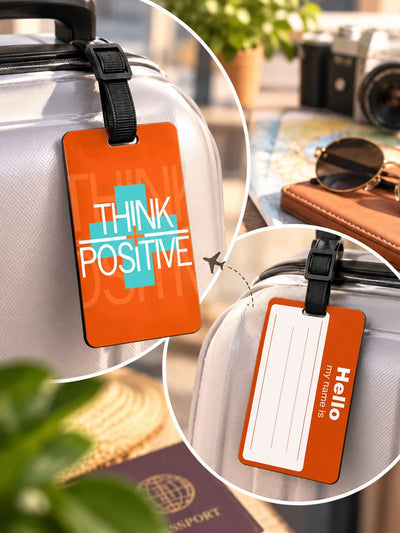 Orange luggage tags with black straps shown attached to a silver suitcase in a travel-themed setting. One tag has the words “THINK POSITIVE” with a teal cross graphic, and the other shows a blank “Hello” name field.