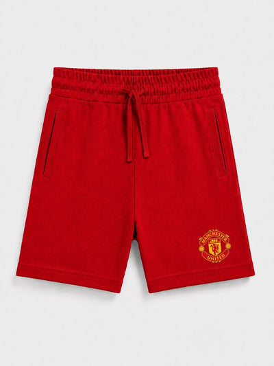 Red sweat shorts with an elastic drawstring waist and a yellow Manchester United crest on the lower left leg, shown against a light gray background.