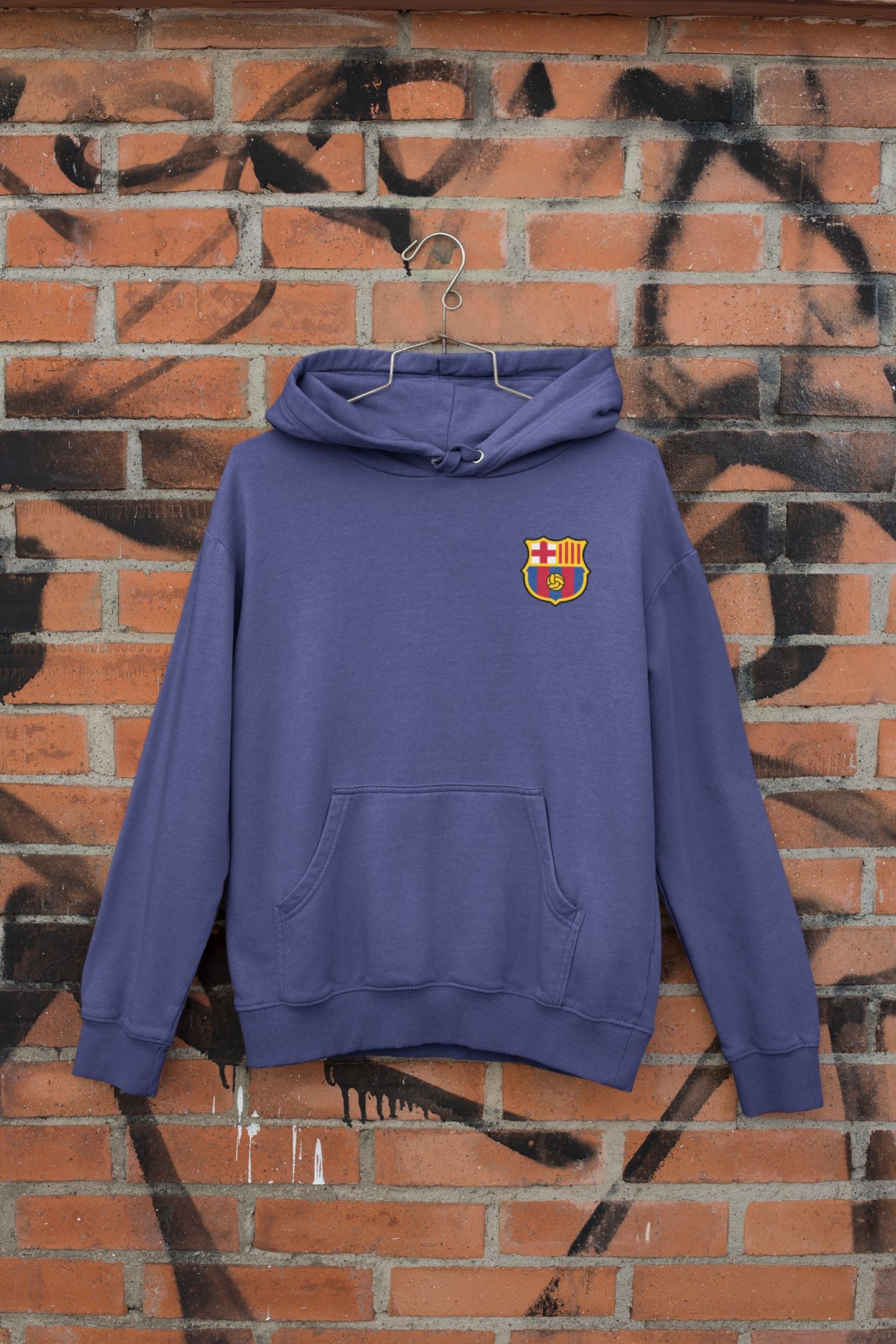 Royal blue hoodie with a logo on a hanger against a graffiti-covered brick wall