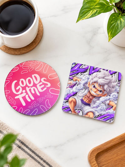 Two printed coasters on a white marble surface with a coffee cup, plant leaves, and a wooden tray nearby. One coaster is round with a pink-to-purple gradient and the words “Good Times” in white.