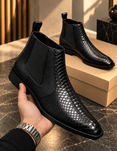 Black Chelsea boot showing croc-texture panels, elastic gusset, and pull tab